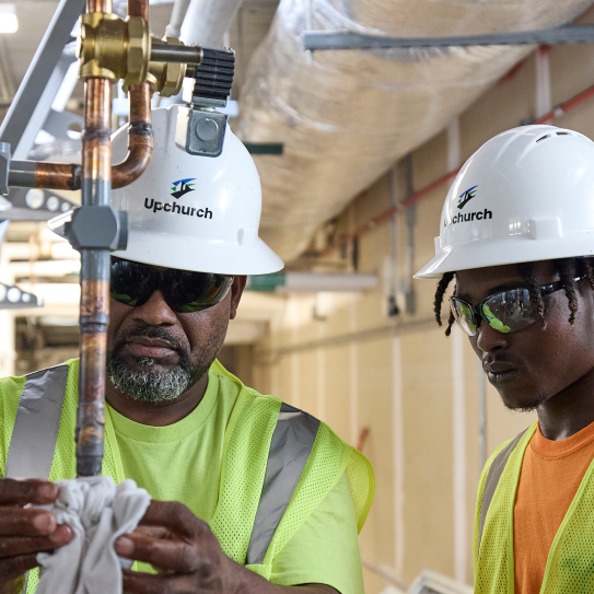 Two Upchurch employees in the field, wearing safety equipment, examining a gas line