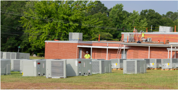 Several rooftop air units in a field in front of a high school